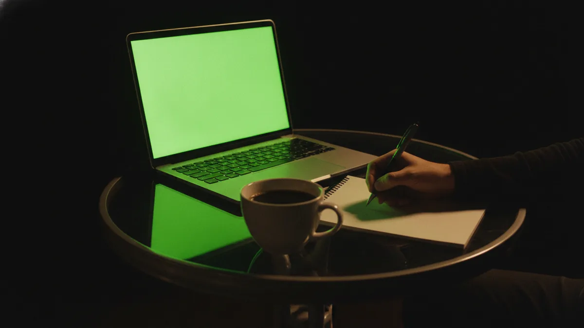Researching logo designers on a laptop with notes at a cafe