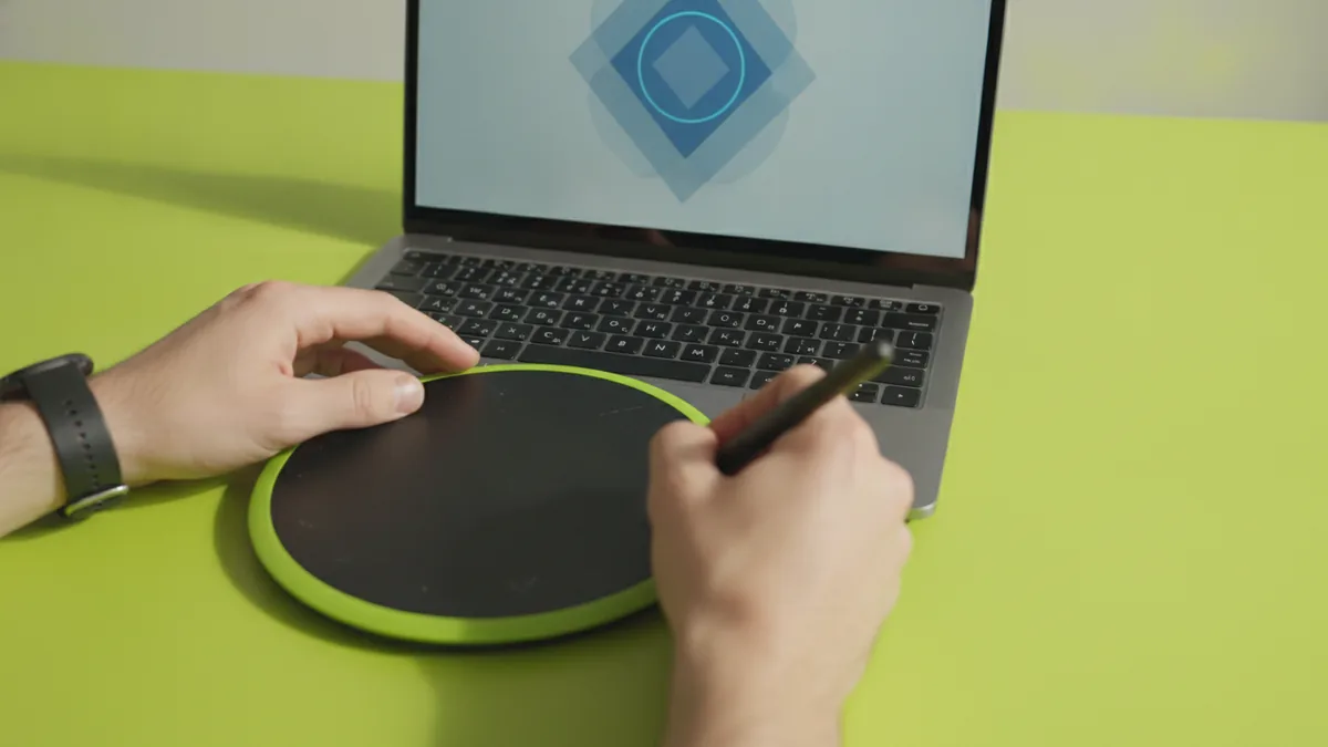 Hands refining a logo cutout on a graphics tablet for a transparent export.
